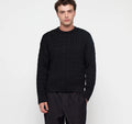 Eine Person trägt einen schwarzen Zopfstrick-Pullover im Boxy Fit mit Rundhalsausschnitt vor hellem Hintergrund. koblenz organic basics