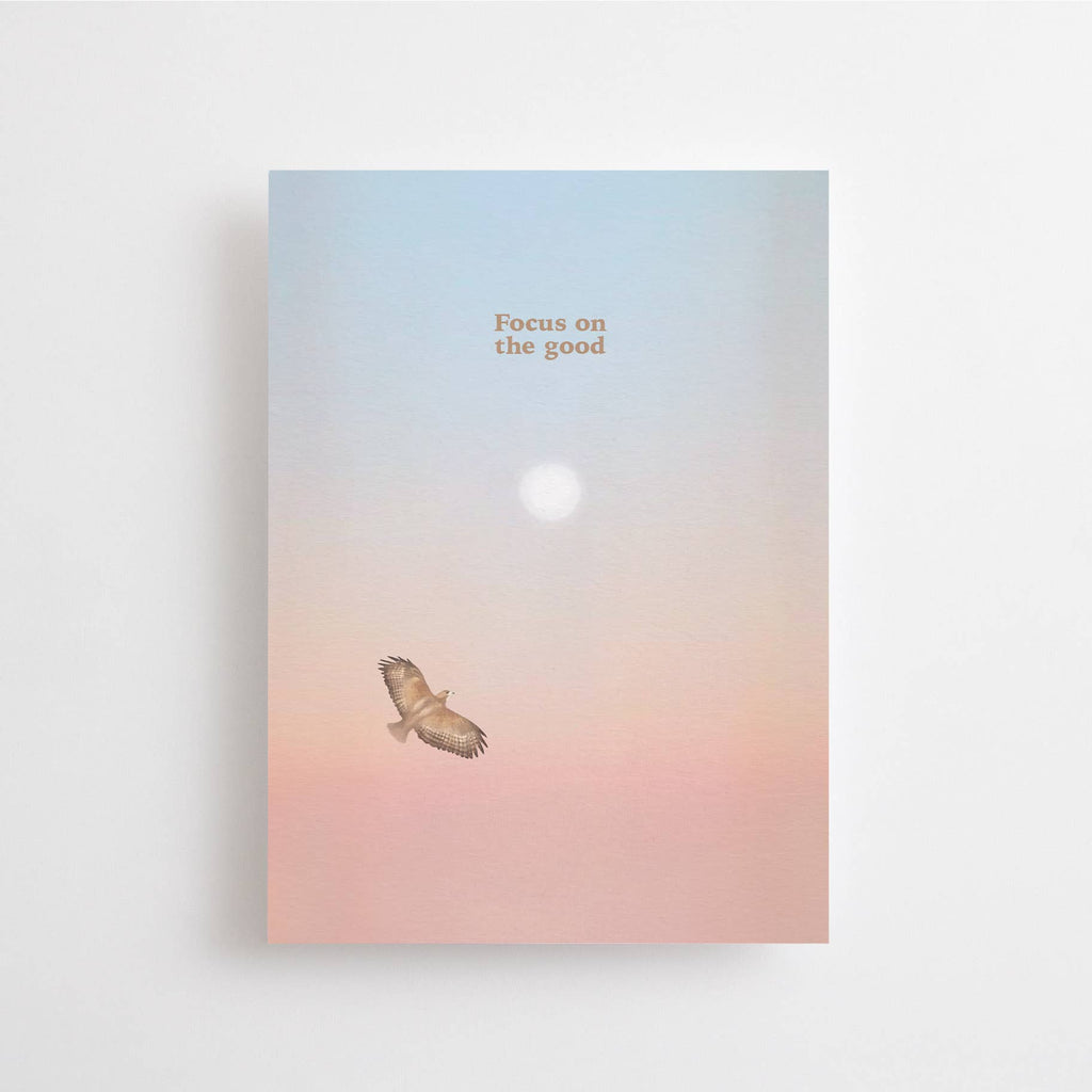 Eine Postkarte mit Rosé-Blau-Farbverlauf, Sonne und fliegendem Greifvogel sowie dem Schriftzug FOCUS ON THE GOOD.