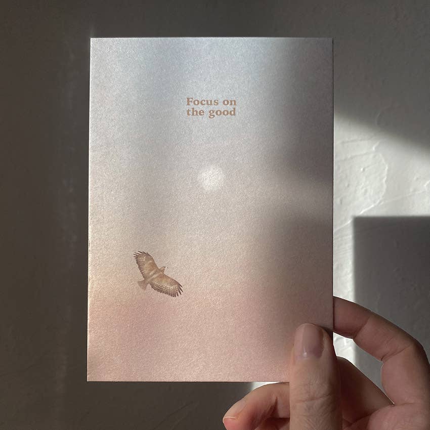 Eine Postkarte mit Rosé-Blau-Farbverlauf, Sonne und fliegendem Greifvogel sowie dem Schriftzug FOCUS ON THE GOOD. koblenz