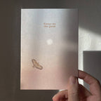 Eine Postkarte mit Rosé-Blau-Farbverlauf, Sonne und fliegendem Greifvogel sowie dem Schriftzug FOCUS ON THE GOOD. koblenz