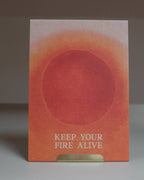 Eine Postkarte mit warmem terracottafarbenem Sonnenmotiv und dem englischen Schriftzug KEEP YOUR FIRE ALIVE auf feinstrukturierte Naturpapier.