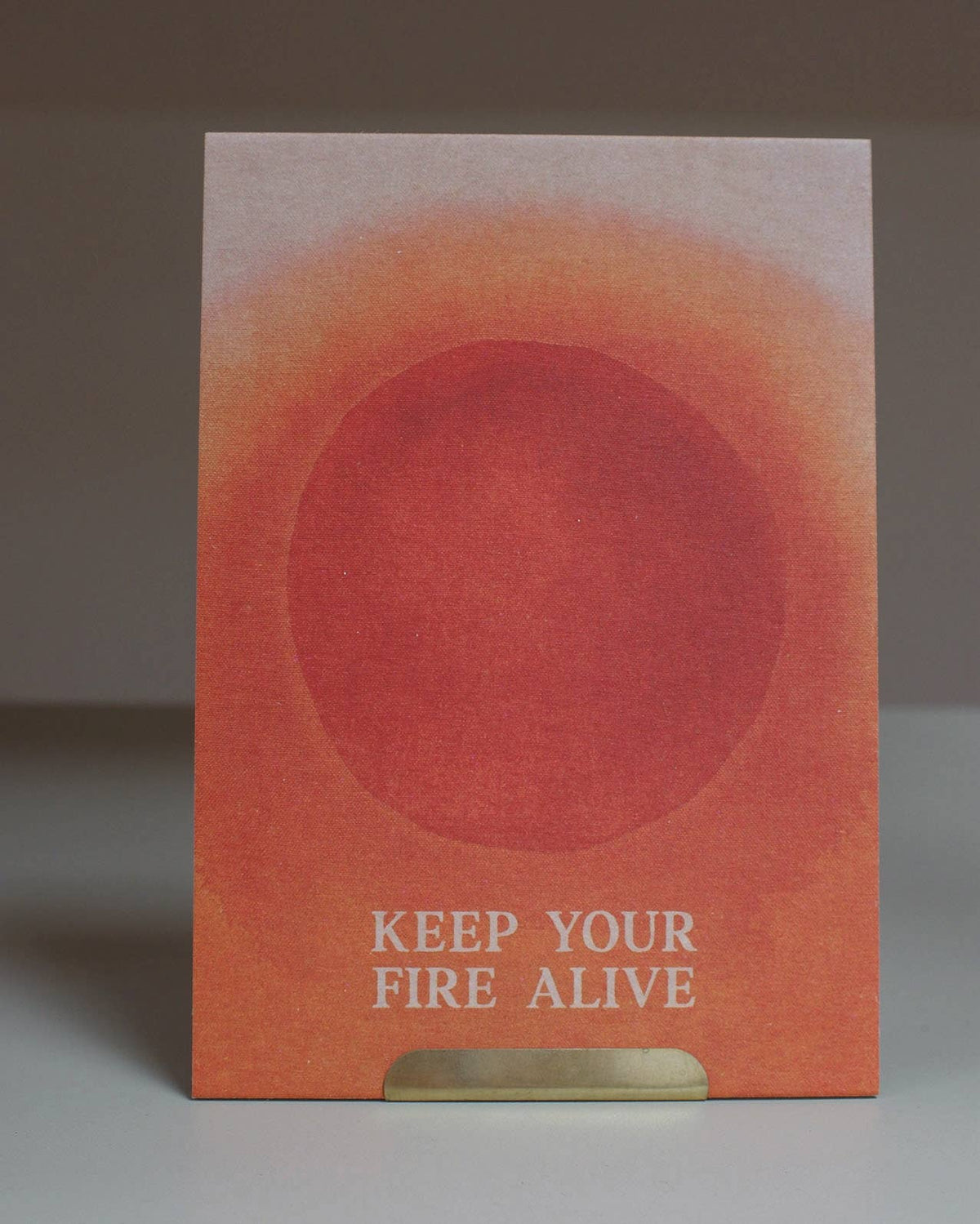 Eine Postkarte mit warmem terracottafarbenem Sonnenmotiv und dem englischen Schriftzug KEEP YOUR FIRE ALIVE auf feinstrukturierte Naturpapier.