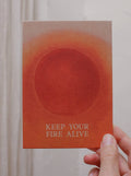 Eine Postkarte mit warmem terracottafarbenem Sonnenmotiv und dem englischen Schriftzug KEEP YOUR FIRE ALIVE auf feinstrukturierte Naturpapier.