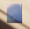 Eine Postkarte von Anna Cosma mit indigoblauem Farbverlauf, strahlendem Augen-Symbol und der englischen Aufschrift „It's already yours“.
