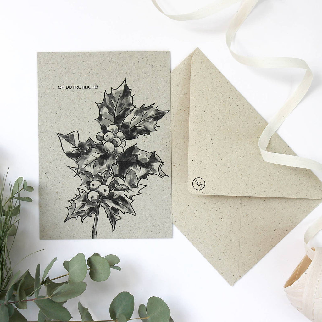Eine Weihnachtskarte aus naturbelassenem Graspapier mit handgezeichnetem Stechpalmenzweig und dem Schriftzug „OH DU FRÖHLICHE!“ 