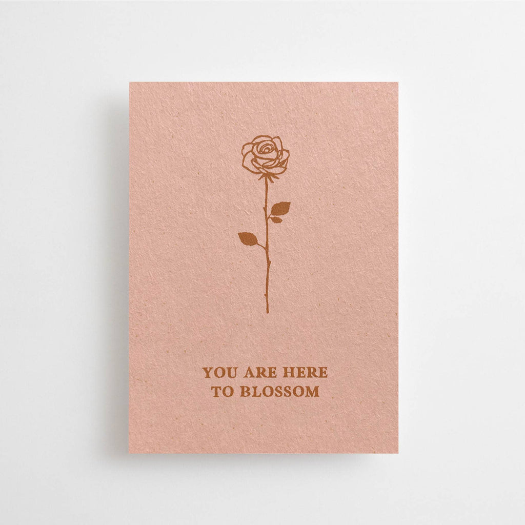 Eine altrosafarbene Mini-Karte mit einer feinen Rosen-Illustration und dem englischen Schriftzug „YOU ARE HERE TO BLOSSOM“ vor weißem Hintergrund.