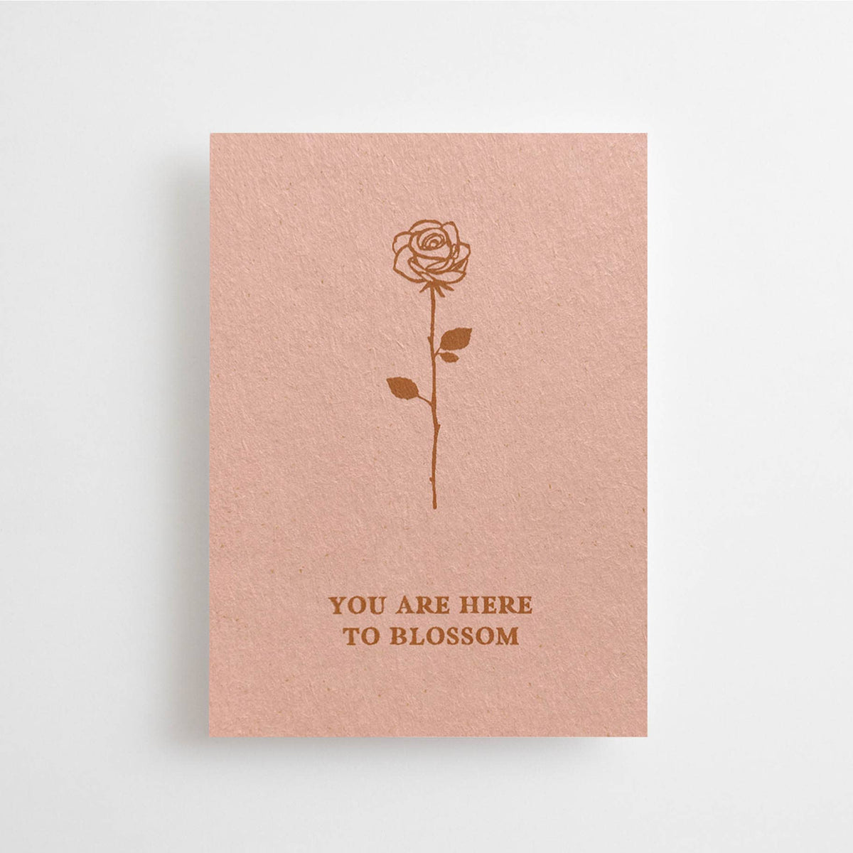 Eine altrosafarbene Mini-Karte mit einer feinen Rosen-Illustration und dem englischen Schriftzug „YOU ARE HERE TO BLOSSOM“ vor weißem Hintergrund.
