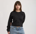 Eine brünette Frau trägt ein schwarzes, kastig geschnittenes Boxy-Sweatshirt mit Rundhalsausschnitt und Blue Jeans vor hellem Hintergrund.