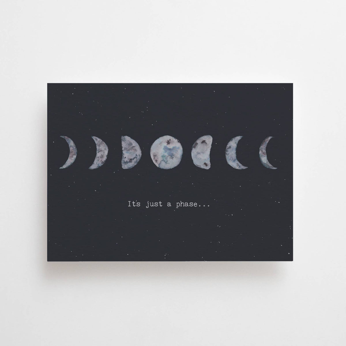 Eine dunkelgraue Postkarte von Anna Cosma im Querformat mit illustrierten Mondphasen und der englischen Aufschrift „It's just a phase...“.