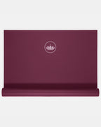 Gefaltete weinrote Yogamatte "Arise Travel" in Dark Cranberry mit Lotus-Logo vor hellem Hintergrund.