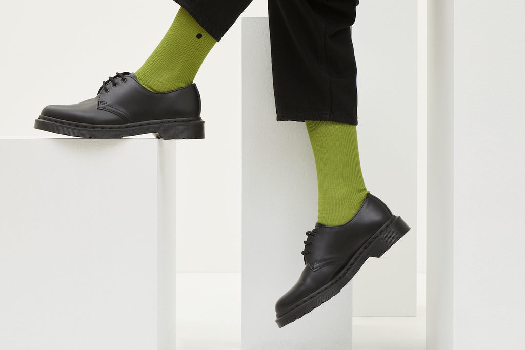 Grüne Socken Luji im Rippstrick-Design mit nahtloser Fußspitze, abgebildet als flach liegendes Produkt und getragen mit schwarzen Schuhen.