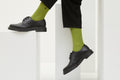 Grüne Socken Luji im Rippstrick-Design mit nahtloser Fußspitze, abgebildet als flach liegendes Produkt und getragen mit schwarzen Schuhen.