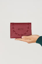 Hand hält die burgunder rote Ledergeldbörse "Elea" mit geprägtem SKFK-Logo vor hellem Hintergrund.