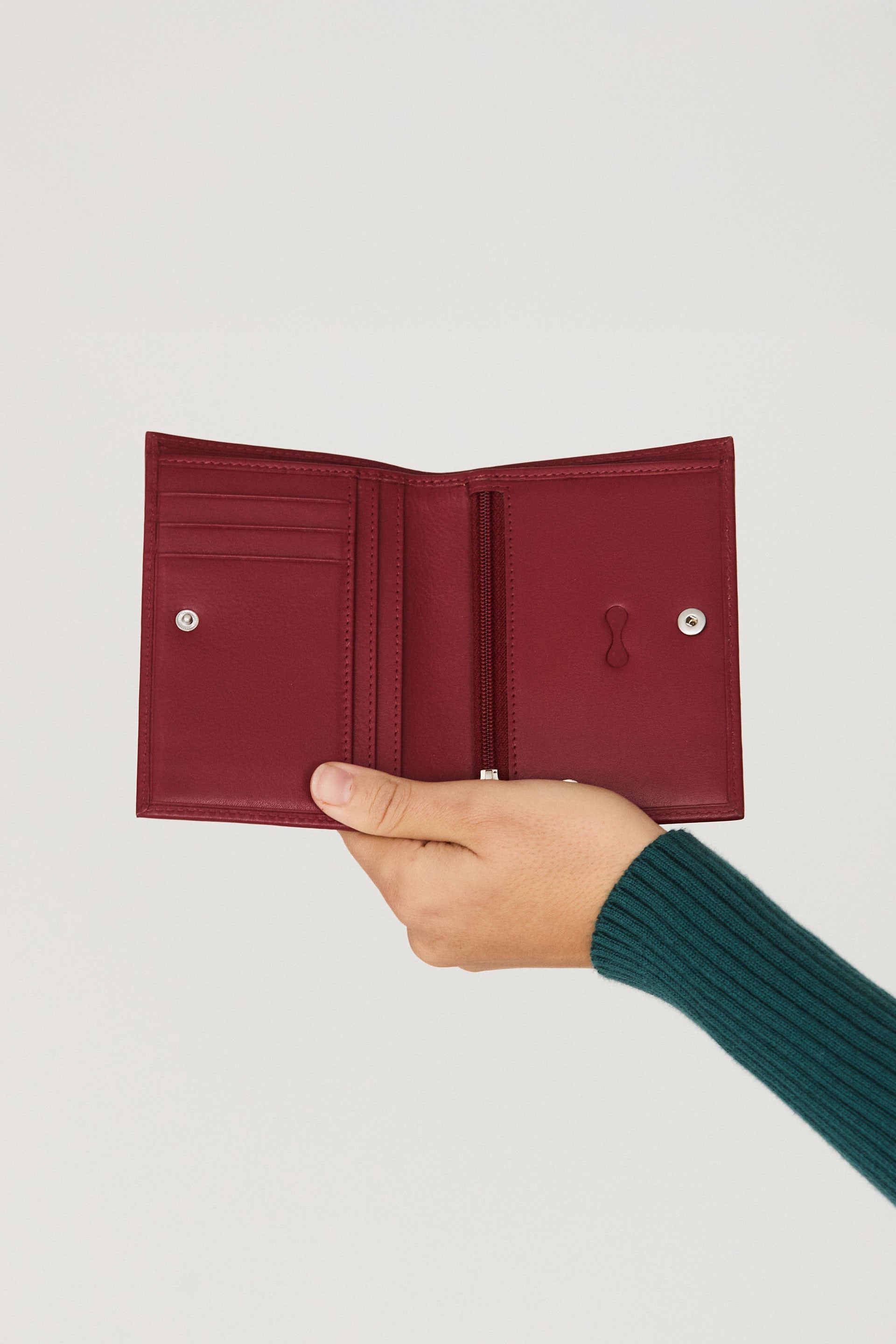 Hand hält die burgunder rote Ledergeldbörse "Elea" mit geprägtem SKFK-Logo vor hellem Hintergrund.