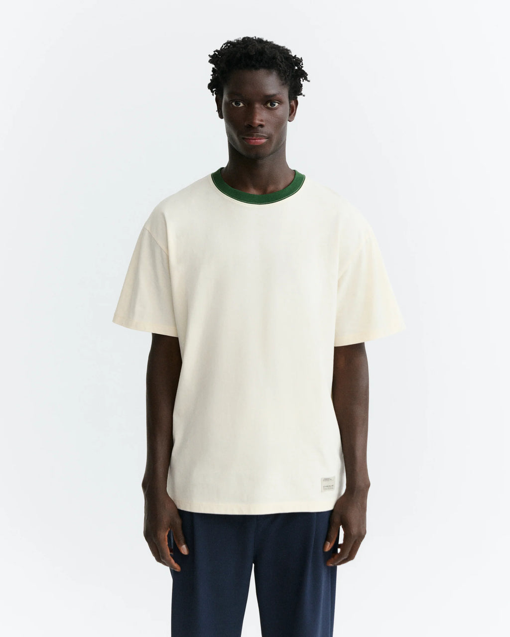 Person von hinten in einem hellen T-Shirt "Aaron" mit grünem Pirineo-Print auf der Rückseite und kontrastfarbenem grünen Rippkragen vor hellem Hintergrund.