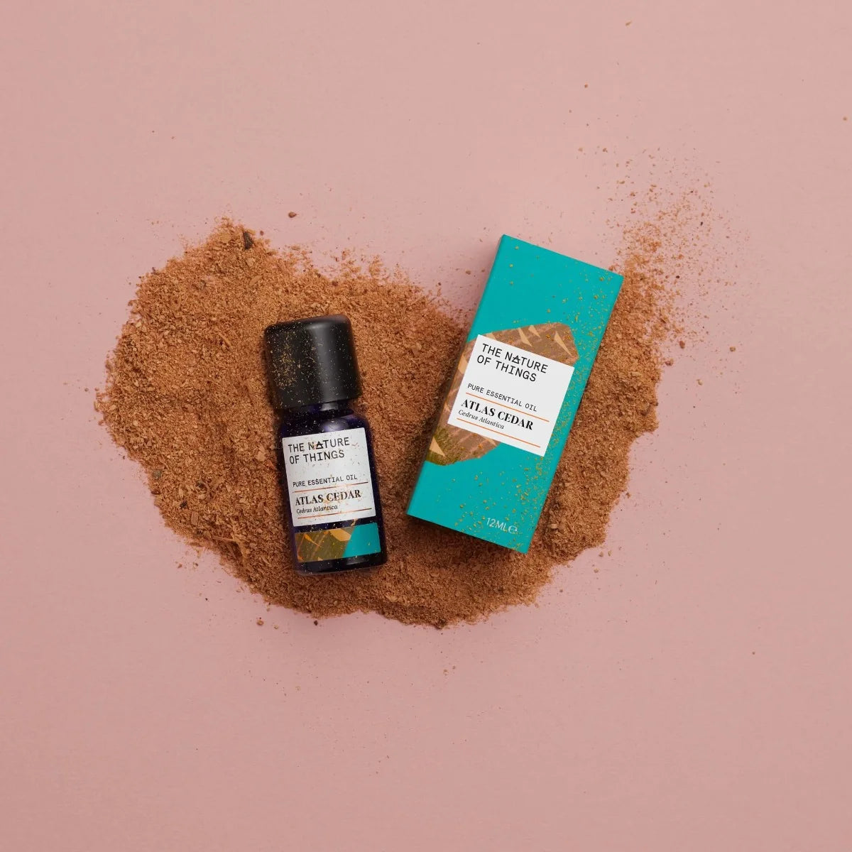 Kleine blaue 12-ml-Flasche des Essential Oil Cedar von The Nature of Things und dazugehörige türkisblaue Umverpackung mit Holzdarstellung vor einem hellblauen Hintergrund.