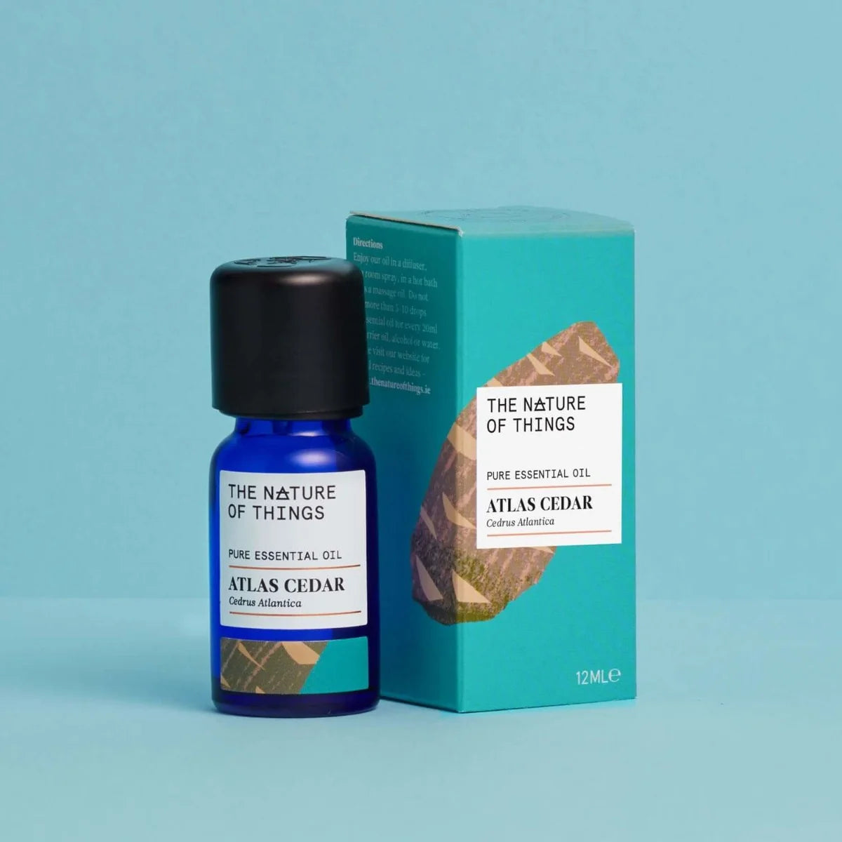 Kleine blaue 12-ml-Flasche des Essential Oil Cedar von The Nature of Things und dazugehörige türkisblaue Umverpackung mit Holzdarstellung vor einem hellblauen Hintergrund.