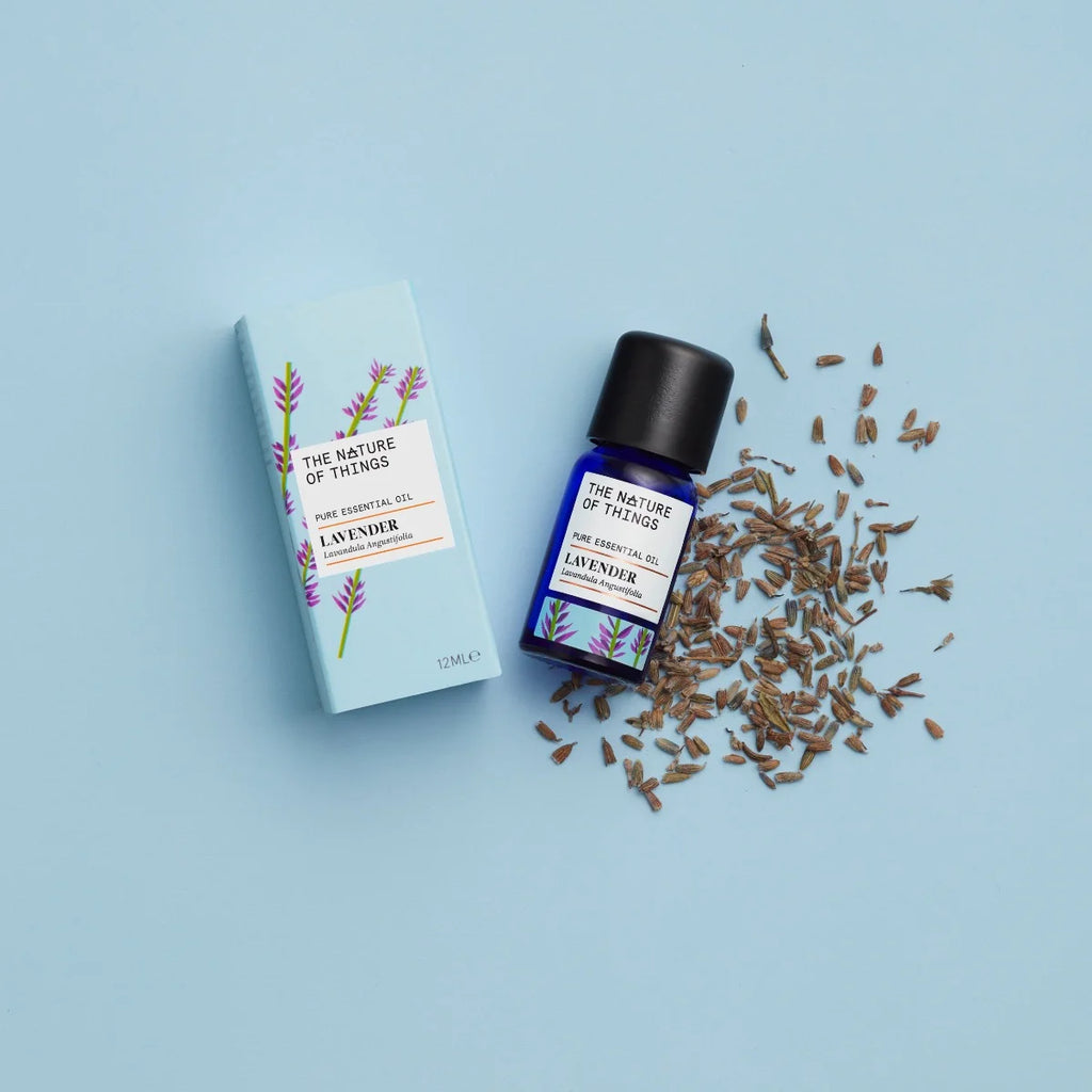 Kleine blaue 12-ml-Flasche des Essential Oil Lavender von The Nature of Things und dazugehörige hellblaue Umverpackung mit Lavendel-Illustrationen vor einem hellblauen Hintergrund.