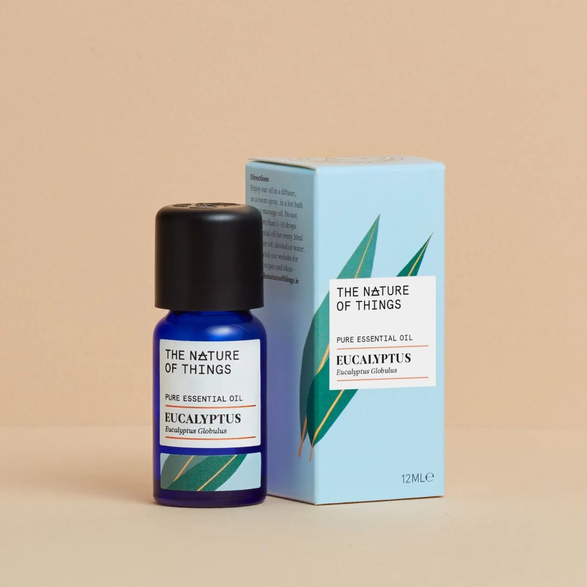 Kleine blaue 12-ml-Flasche des Essential Oil Organic Eucalyptus von The Nature of Things und dazugehörige hellblaue Umverpackung mit Eukalyptus-Illustrationen vor einem beigen Hintergrund.