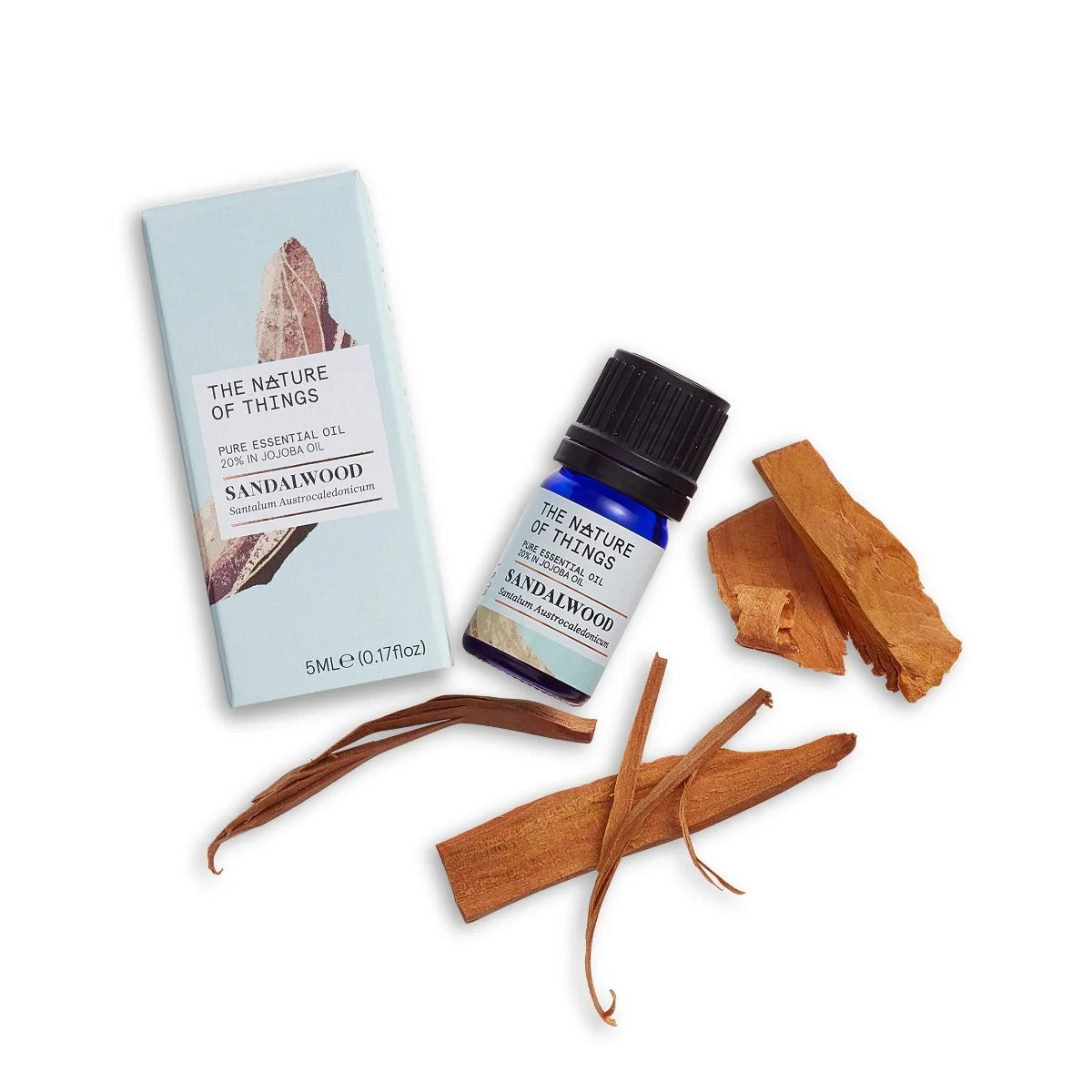 Kleine blaue 5-ml-Flasche des Essential Oil Sandalwood von The Nature of Things und dazugehörige hellblaue Umverpackung mit Holzdarstellung vor einem grünen Hintergrund.
