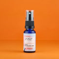 Kleine blaue Sprühflasche des Rose Mists von The Nature of Things mit rosa-weißem Etikett und durchsichtigem Sprühkopf auf orangefarbenem Hintergrund.