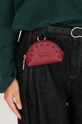 Kleine rote Geldbörse "Nea" mit geprägtem SKFK-Logo und Karabiner, befestigt an einer Gürtelschlaufe über einer dunklen Jeans.