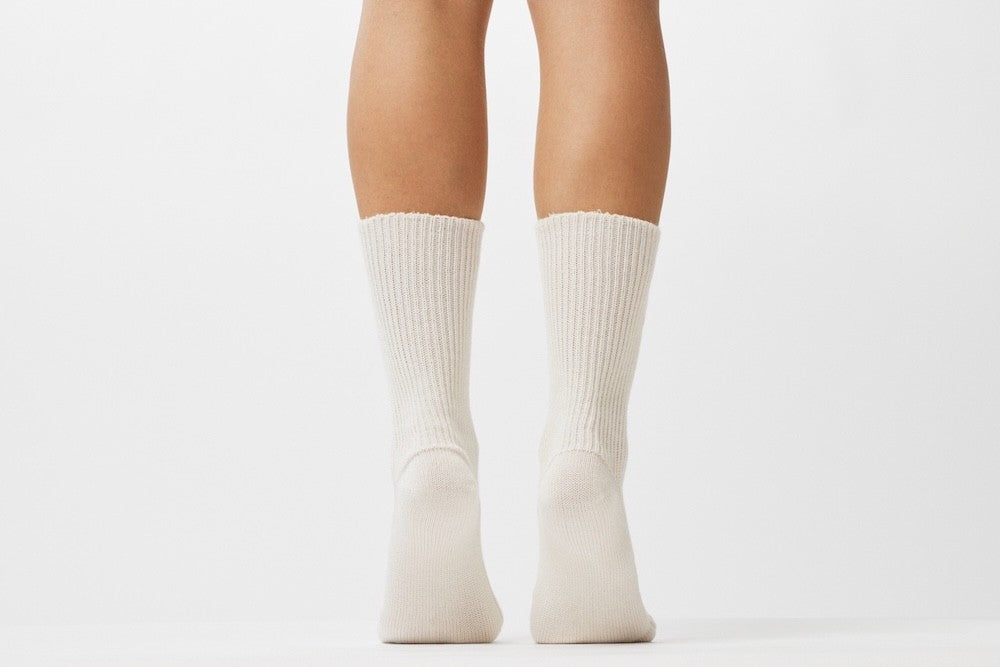 Kobenz; Ein Paar gestrickte Socken aus Wolle in meliertem Cremeweiß vor weißem Hintergrund.