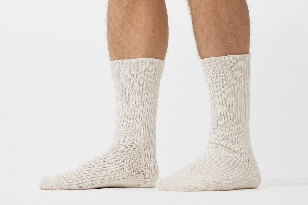 Kobenz; Ein Paar gestrickte Socken aus Wolle in meliertem Cremeweiß vor weißem Hintergrund. trust 