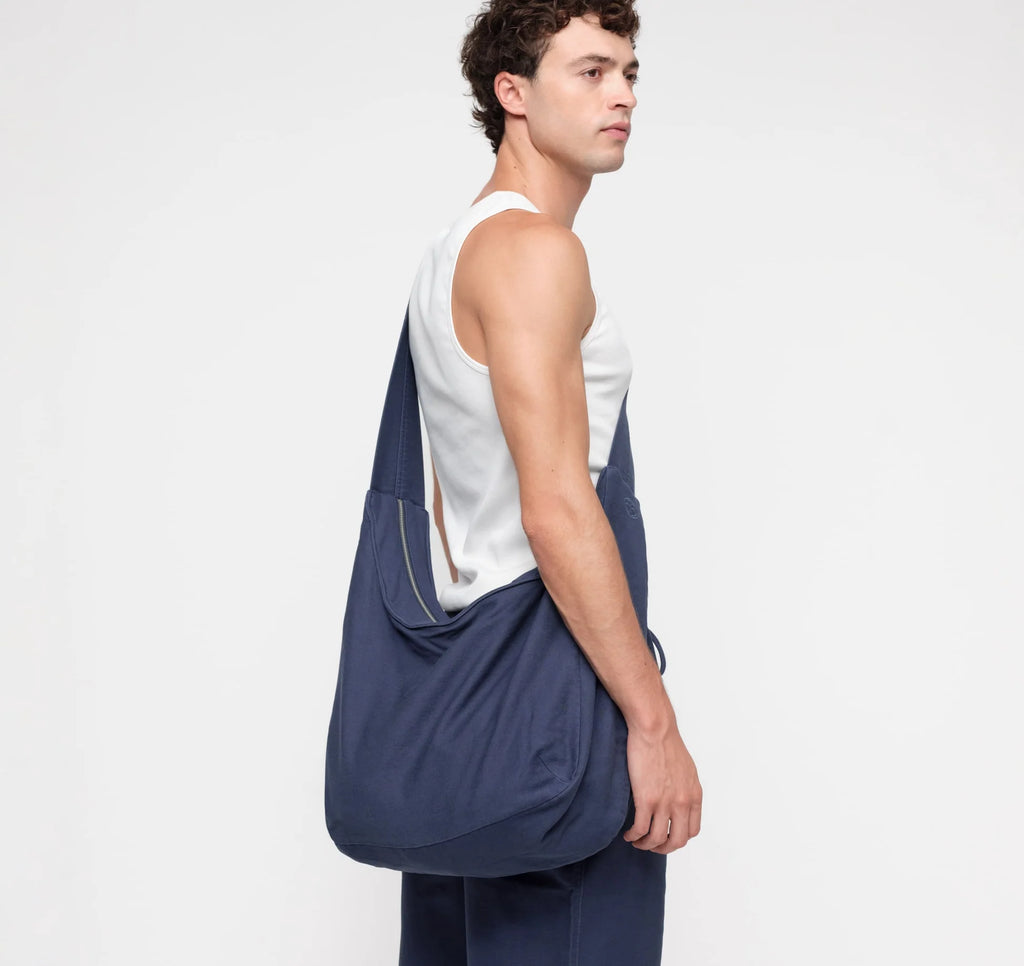 Männliches Model trägt die dunkelblaue Alley Copenhagen Shoulder Bag lässig über der Schulter vor hellem Hintergrund.