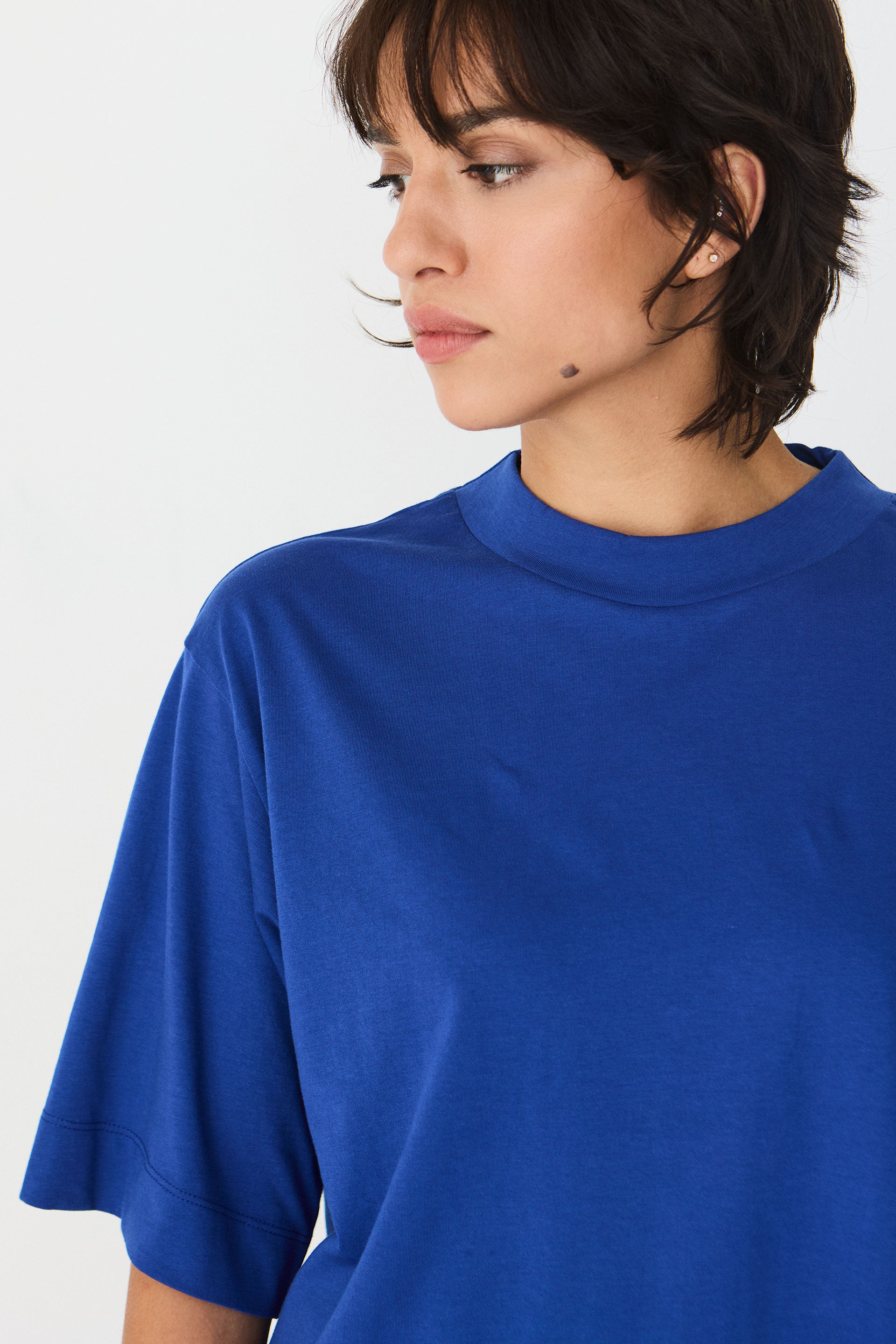 Model trägt das blaue Zuntz-11-Gots T-Shirt der Marke SKFK mit Stehkragen und kurzen Ärmeln zu hellen Hosen.