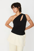 Model trägt das schwarze Kris-Gots T-Shirt der Marke SKFK im One-Shoulder-Stil mit Keyhole-Ausschnitt zu einem hellen Rock.