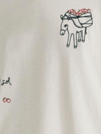 Model trägt das weiße Tomatera White Lena Tee von Thinking Mu mit detailreicher Stickerei eines Esels und Tomaten auf der Brust zu dunkler Hose.