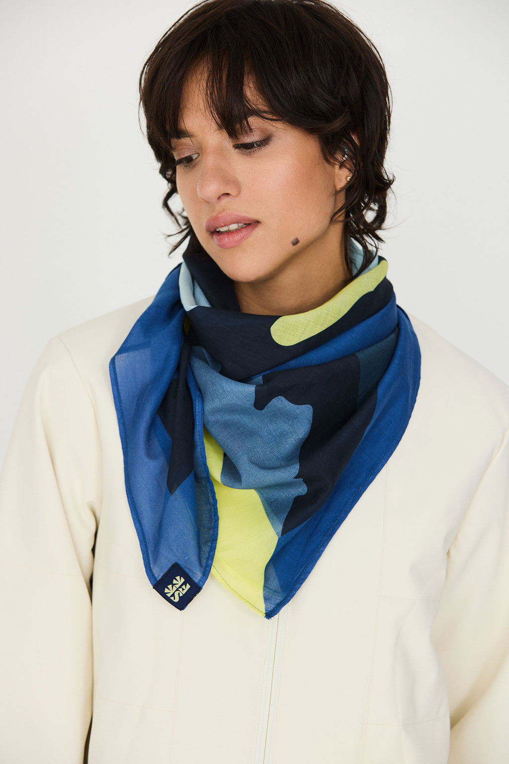 Model trägt den bunten Irura-Gots Scarf von SKFK mit markantem Print elegant um den Hals gebunden zu einem hellen Oberteil.