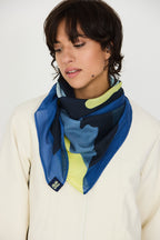 Model trägt den bunten Irura-Gots Scarf von SKFK mit markantem Print elegant um den Hals gebunden zu einem hellen Oberteil.