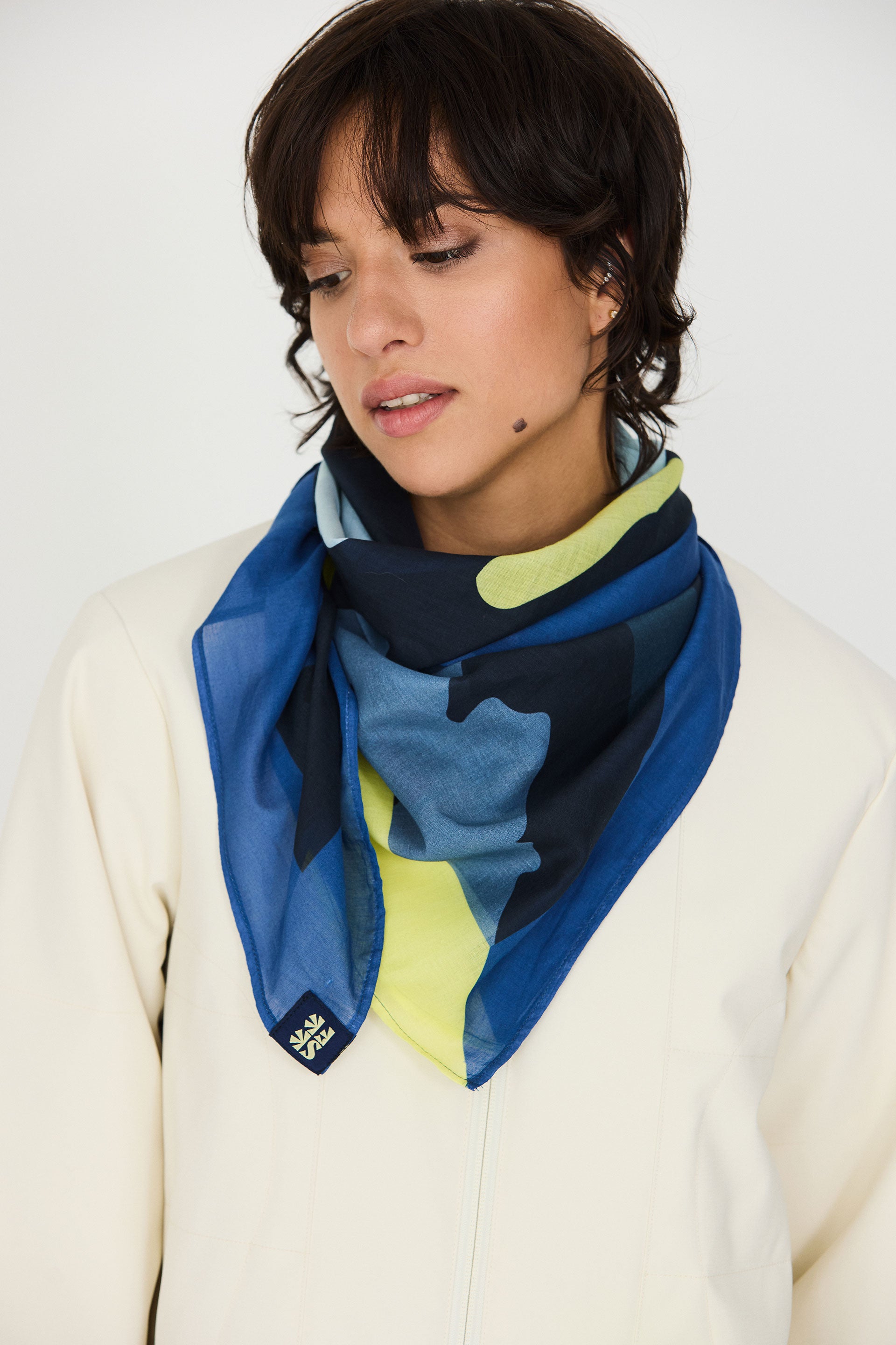 Model trägt den bunten Irura-Gots Scarf von SKFK mit markantem Print elegant um den Hals gebunden zu einem hellen Oberteil.