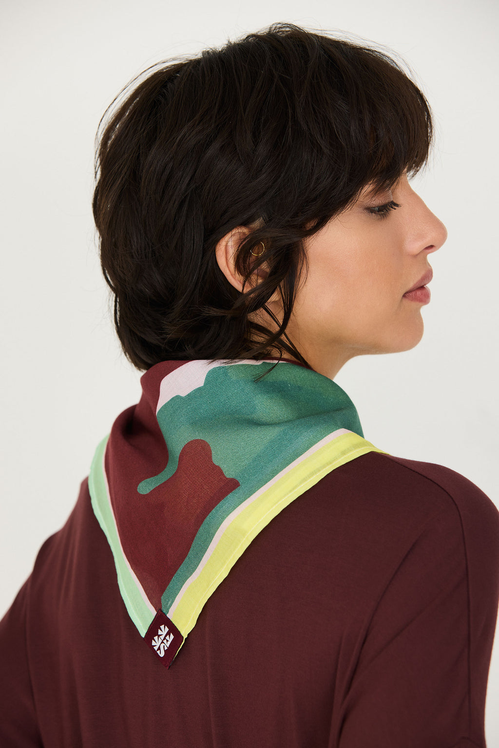 Model trägt den bunten Orbana-Gots Scarf von SKFK mit lebendigem Print elegant um den Hals gebunden zu einem dunkelroten Oberteil.