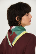 Model trägt den bunten Orbana-Gots Scarf von SKFK mit lebendigem Print elegant um den Hals gebunden zu einem dunkelroten Oberteil.