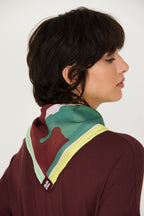 Model trägt den bunten Orbana-Gots Scarf von SKFK mit lebendigem Print elegant um den Hals gebunden zu einem dunkelroten Oberteil.