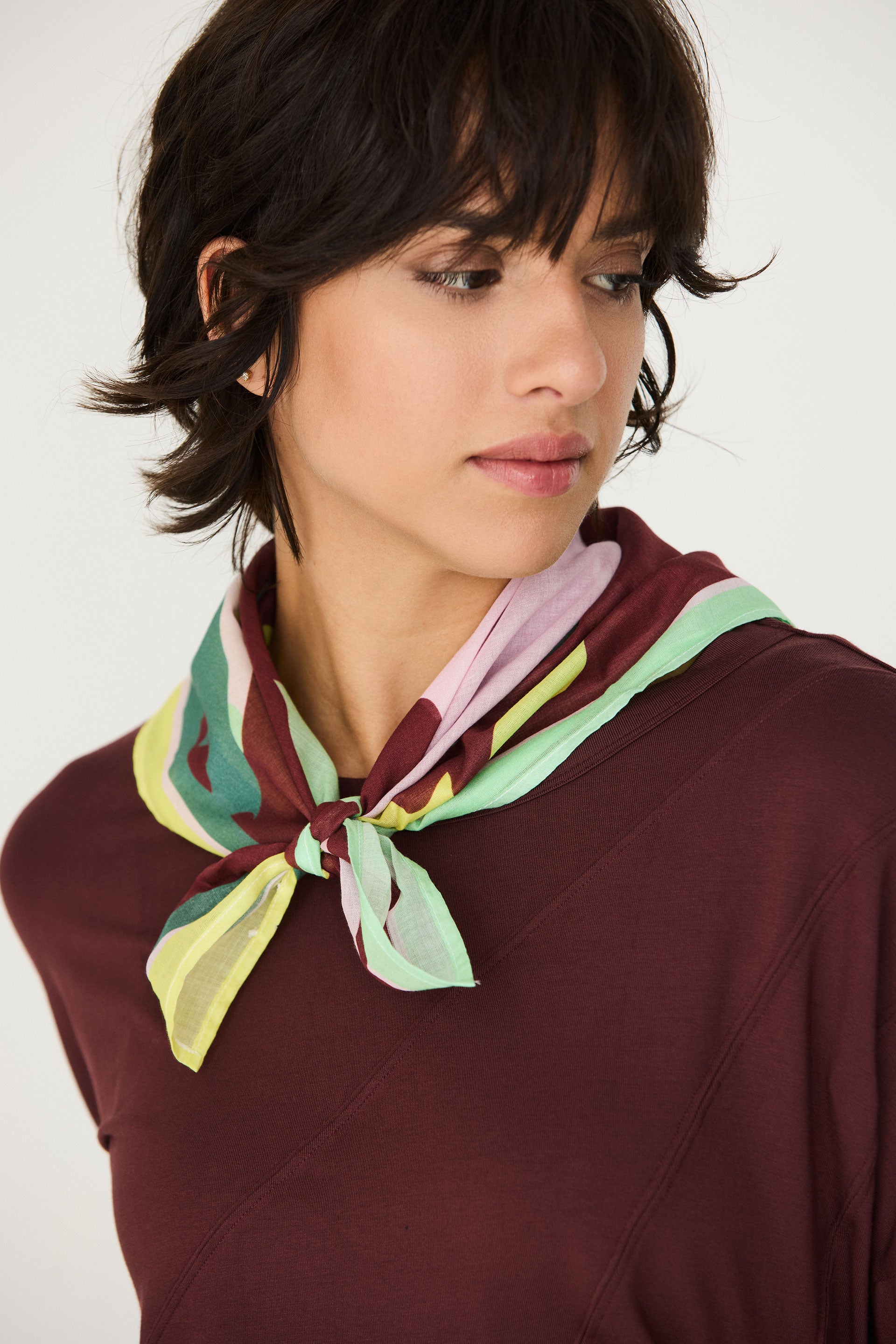 Model trägt den bunten Orbana-Gots Scarf von SKFK mit lebendigem Print elegant um den Hals gebunden zu einem dunkelroten Oberteil.