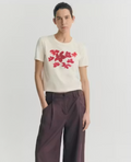 Model trägt ein cremeweißes Red Garden Pannacota Zowie Tee von Thinking Mu mit einem roten floralen Blumenmuster auf der Brust.