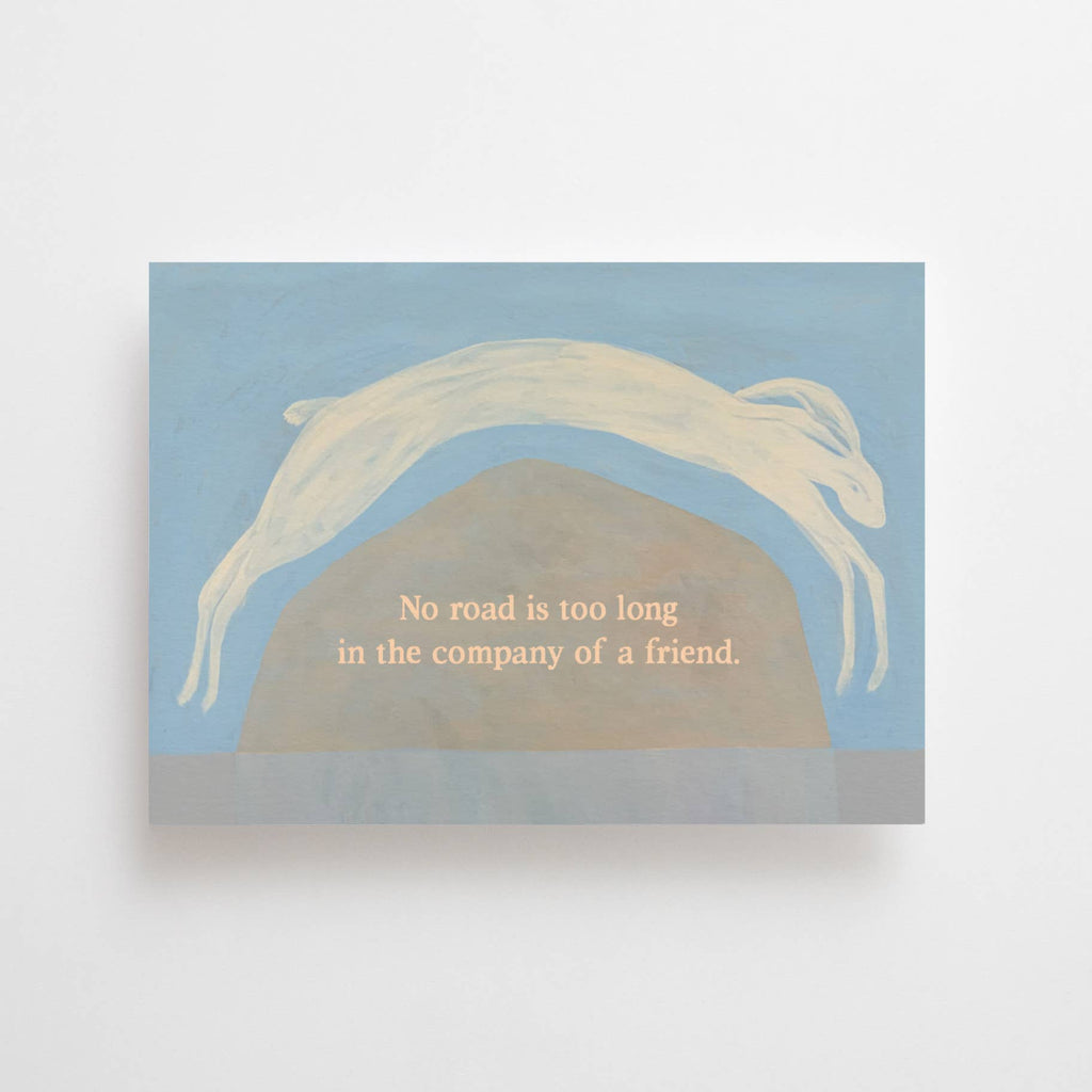 "No Road is too long" im DIN-A6-Format von Anna Cosma mit einem springenden weißen Hasen über eine Hügellandschaft vor blauschattiertem Hintergrund und dem Text „No road is too long in the company of a friend.“.