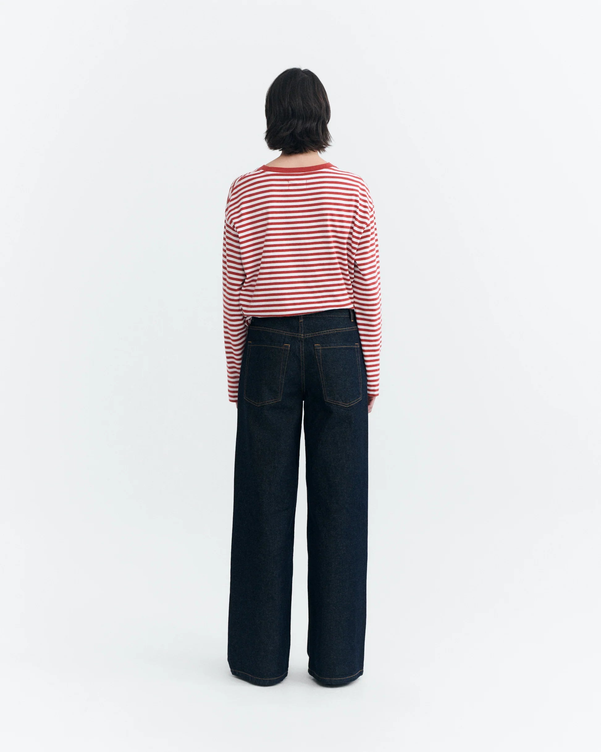 Person trägt die weite blaue Jeans "Hedda" mit weitem Bein und niedrigem Bund in Kombination mit einem rot-weiß gestreiften Langarmshirt vor hellem Hintergrund.