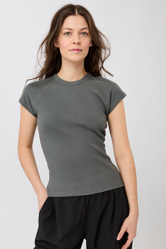 Person von vorne in einem dunkelgrauen, gerippten Slim-Fit-T-Shirt mit kurzen Ärmeln und Raglanschnitt vor hellem Hintergrund.