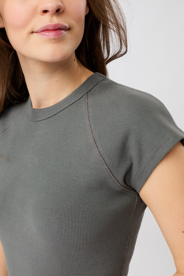 Person von vorne in einem dunkelgrauen, gerippten Slim-Fit-T-Shirt mit kurzen Ärmeln und Raglanschnitt vor hellem Hintergrund.
