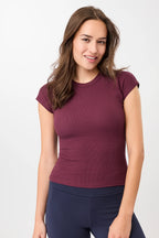 Person von vorne in einem dunkelroten, gerippten Slim-Fit-T-Shirt mit kurzen Ärmeln und Raglanschnitt vor hellem Hintergrund.