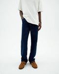 Person von vorne in einer dunklen Straight-Leg Jeans "David" mit hellem Shirt und braunen Schuhen vor hellem Hintergrund.