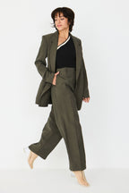 Person von vorne in einer geraden taupefarbenen Hose "Afrika" und einem schwarzen One-Shoulder-Oberteil vor hellem Hintergrund.