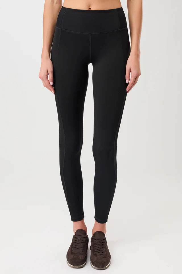 Person von vorne in einer schwarzen High-Rise-Leggings "Limitless" mit dynamischen Teilungsnähten und dunklen Sneakern vor hellem Hintergrund.