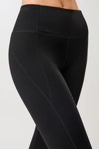 Person von vorne in einer schwarzen High-Rise-Leggings "Limitless" mit dynamischen Teilungsnähten und dunklen Sneakern vor hellem Hintergrund.