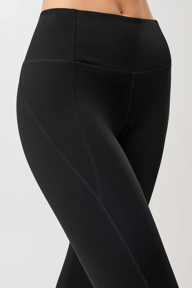 Person von vorne in einer schwarzen High-Rise-Leggings "Limitless" mit dynamischen Teilungsnähten und dunklen Sneakern vor hellem Hintergrund.